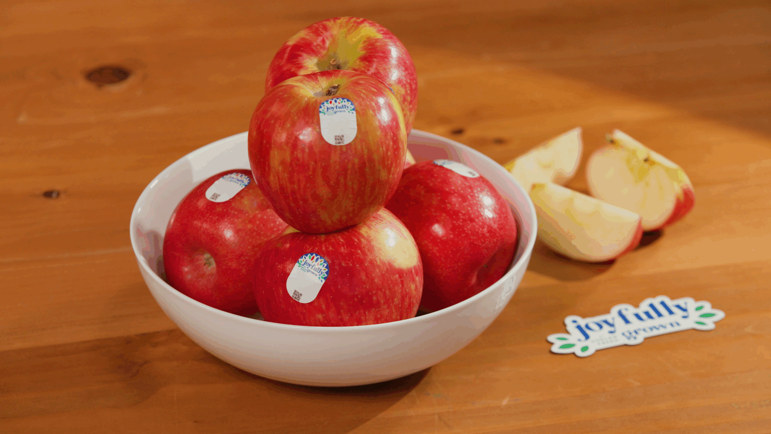 apples in white bowl on wooden counter with Joyfully Grown stickers